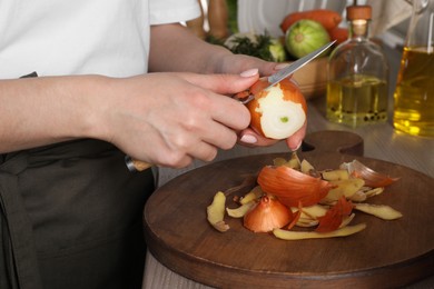 Woman peeling fresh onion with knife at table indoors, closeup