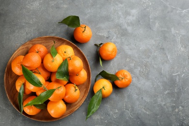 Photo of Fresh tangerines with green leaves on grey table, flat lay. Space for text