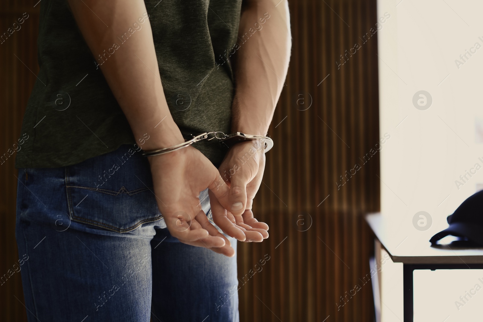 Photo of Man detained in handcuffs indoors, space for text. Criminal law