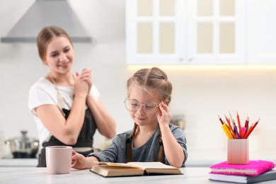 Photo of Happy mother watching her daughter doing homework in kitchen