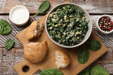 Photo of Tasty spinach dip with egg in bowl, bread and spices on wooden table, top view