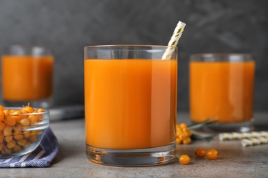 Delicious sea buckthorn juice with straw on grey table, closeup
