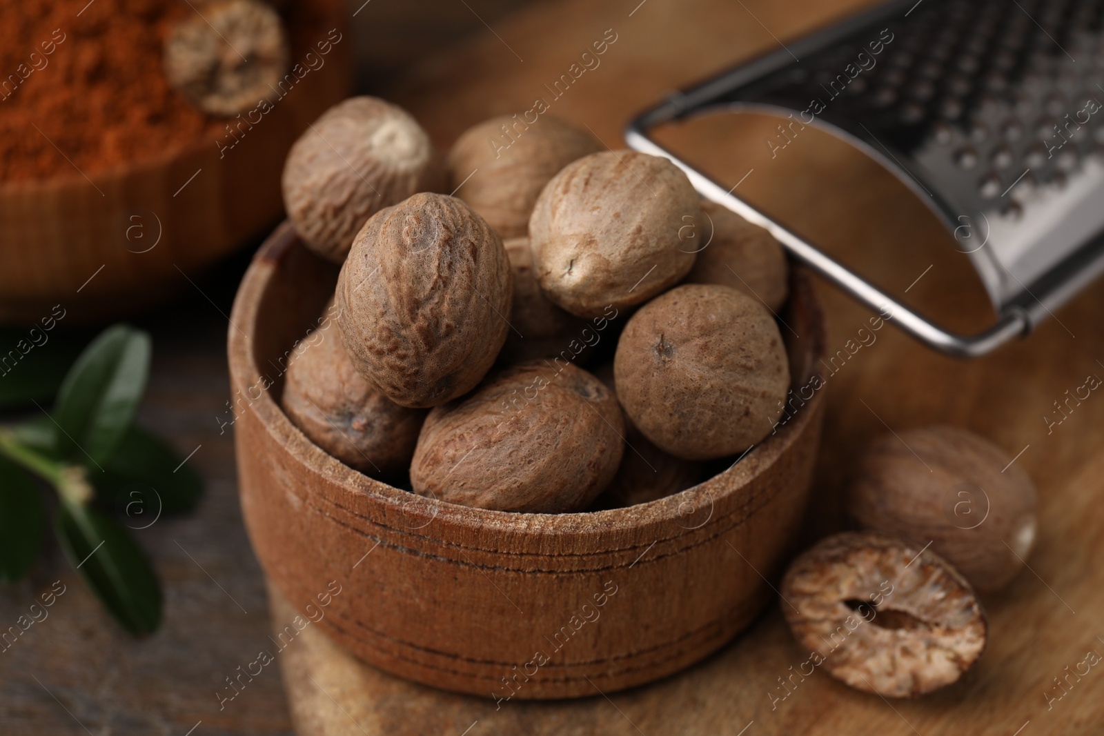 Photo of Nutmegs in bowl and grater on table, closeup