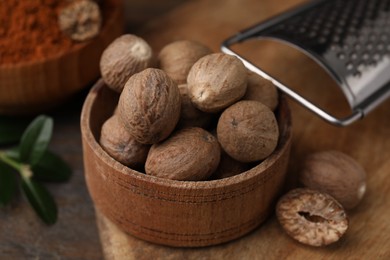 Photo of Nutmegs in bowl and grater on table, closeup