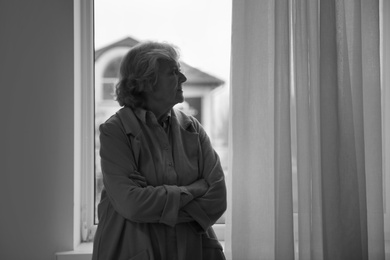 Photo of Portrait of elderly woman near window indoors, space for text. Black and white effect
