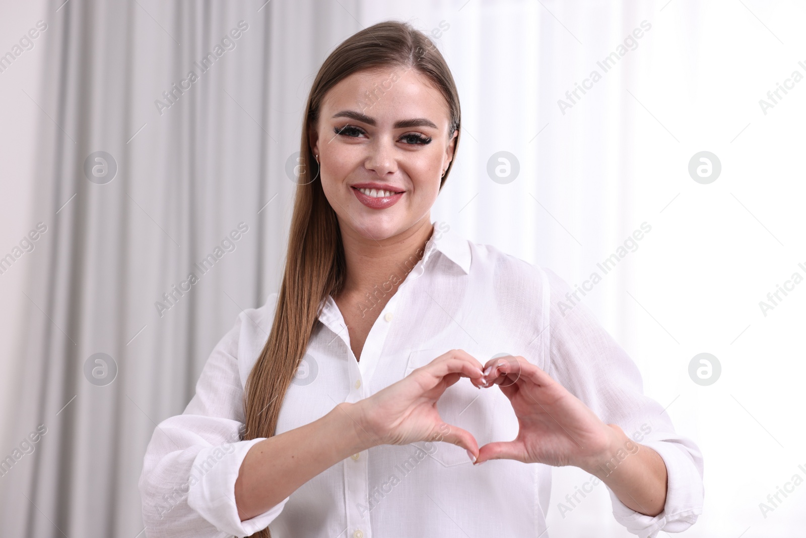 Photo of Happy woman showing heart gesture with hands indoors