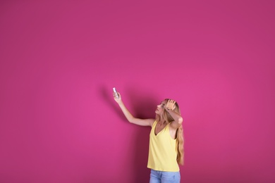 Young woman operating air conditioner with remote control on color background