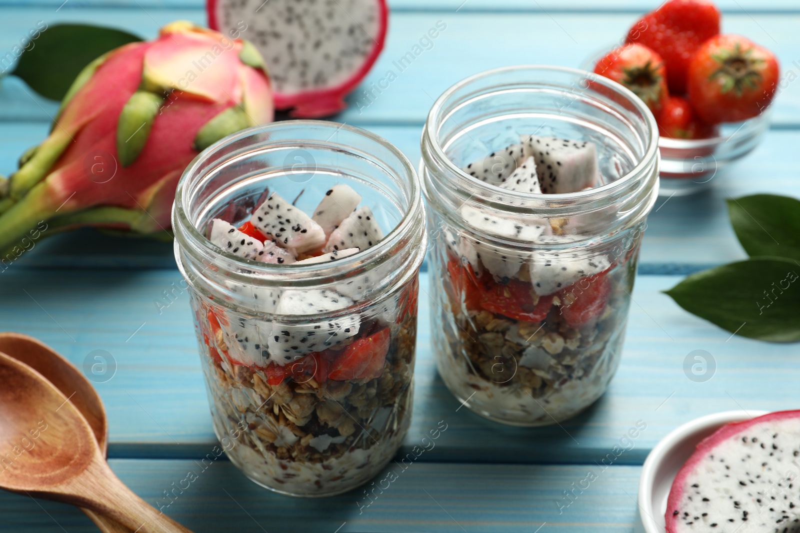 Photo of Granola with strawberries and pitahaya in glass jars on  light blue wooden table