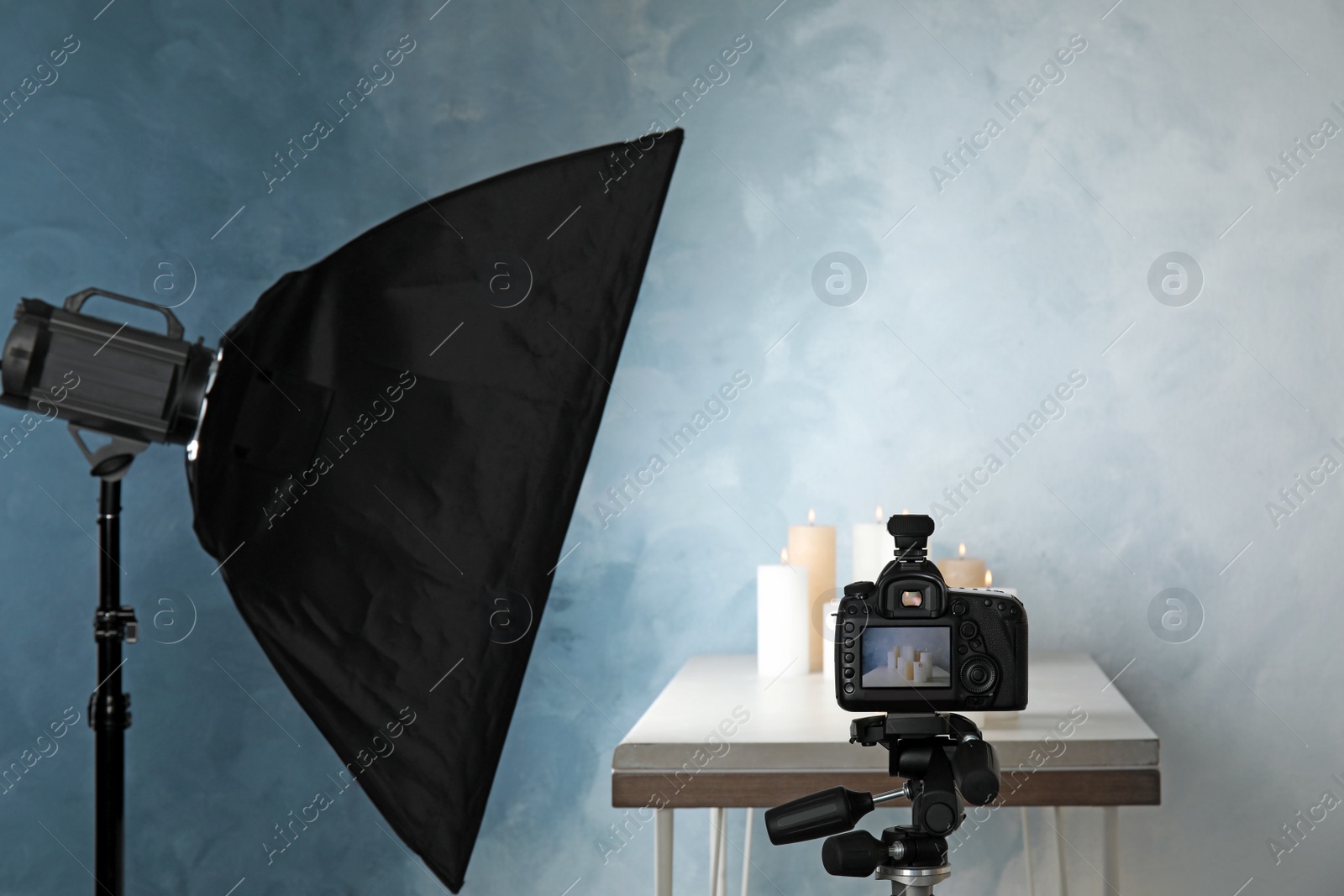 Photo of Professional photo equipment and candles on table against color wall