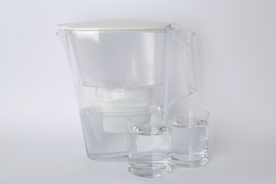 Photo of Filter jug and glasses with purified water on white background