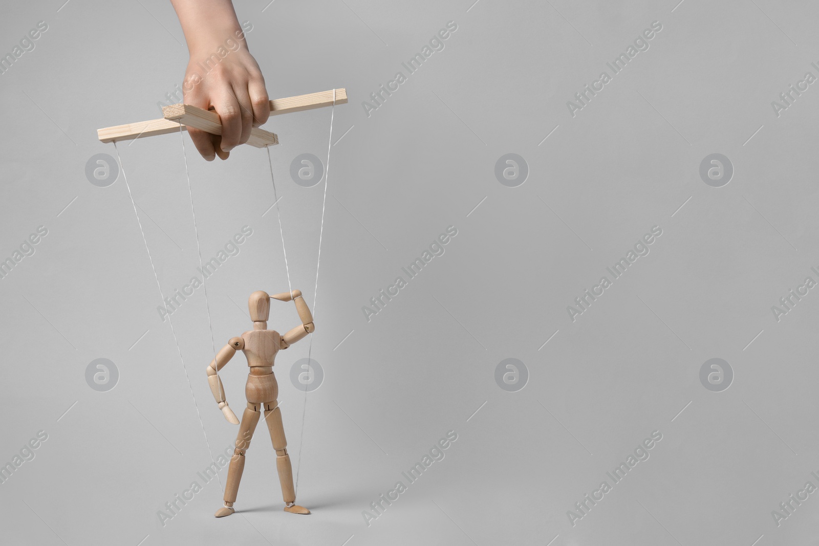 Photo of Woman pulling strings of puppet on light grey background, closeup. Space for text