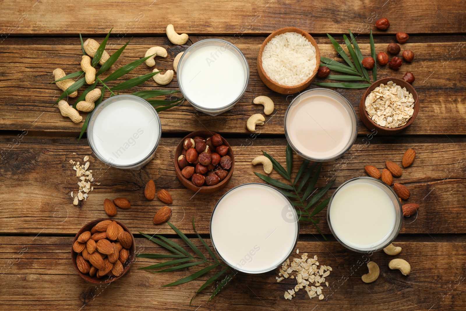 Photo of Different vegan milks and ingredients on wooden table, flat lay