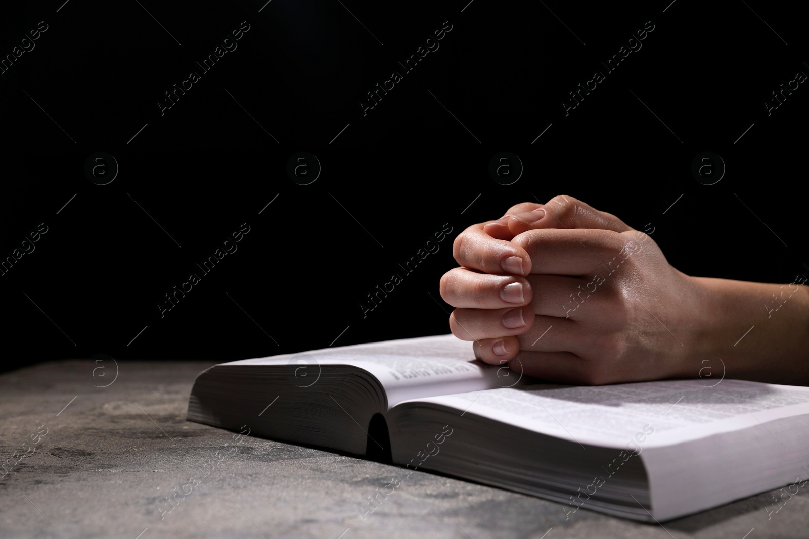 Photo of Religion. Christian woman praying over Bible at table against black background, closeup. Space for text