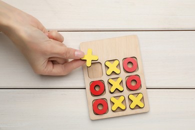 Woman playing tic tac toe game at white wooden table, top view