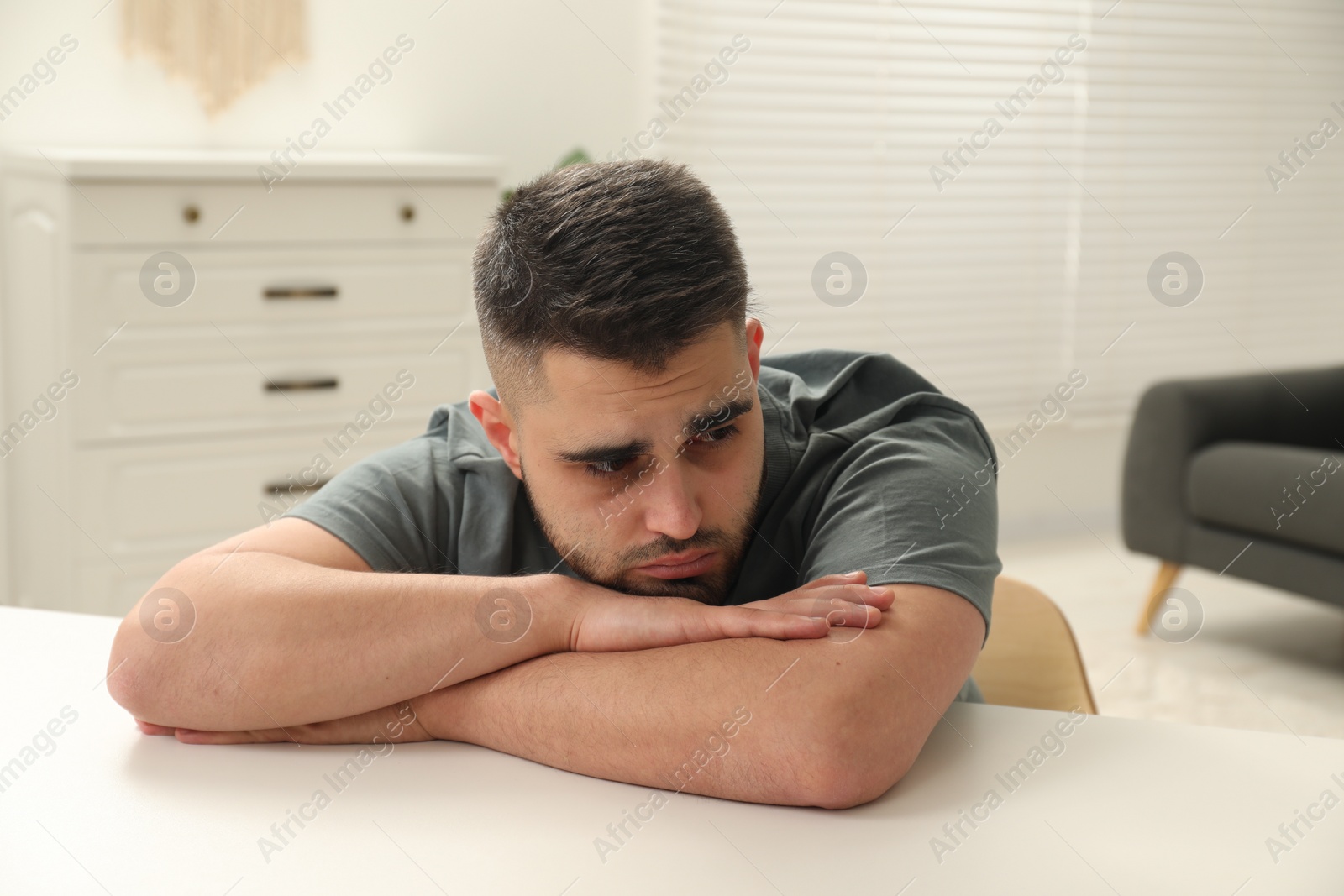 Photo of Sad man sitting at white table indoors