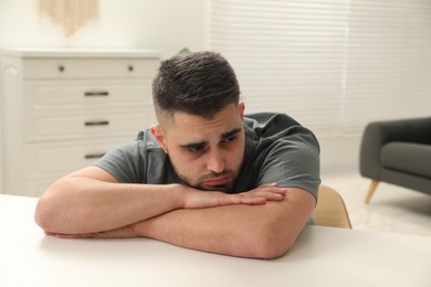 Photo of Sad man sitting at white table indoors