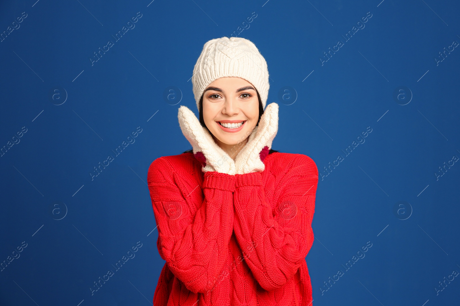 Photo of Young woman wearing warm sweater, mittens and hat on blue background. Winter season