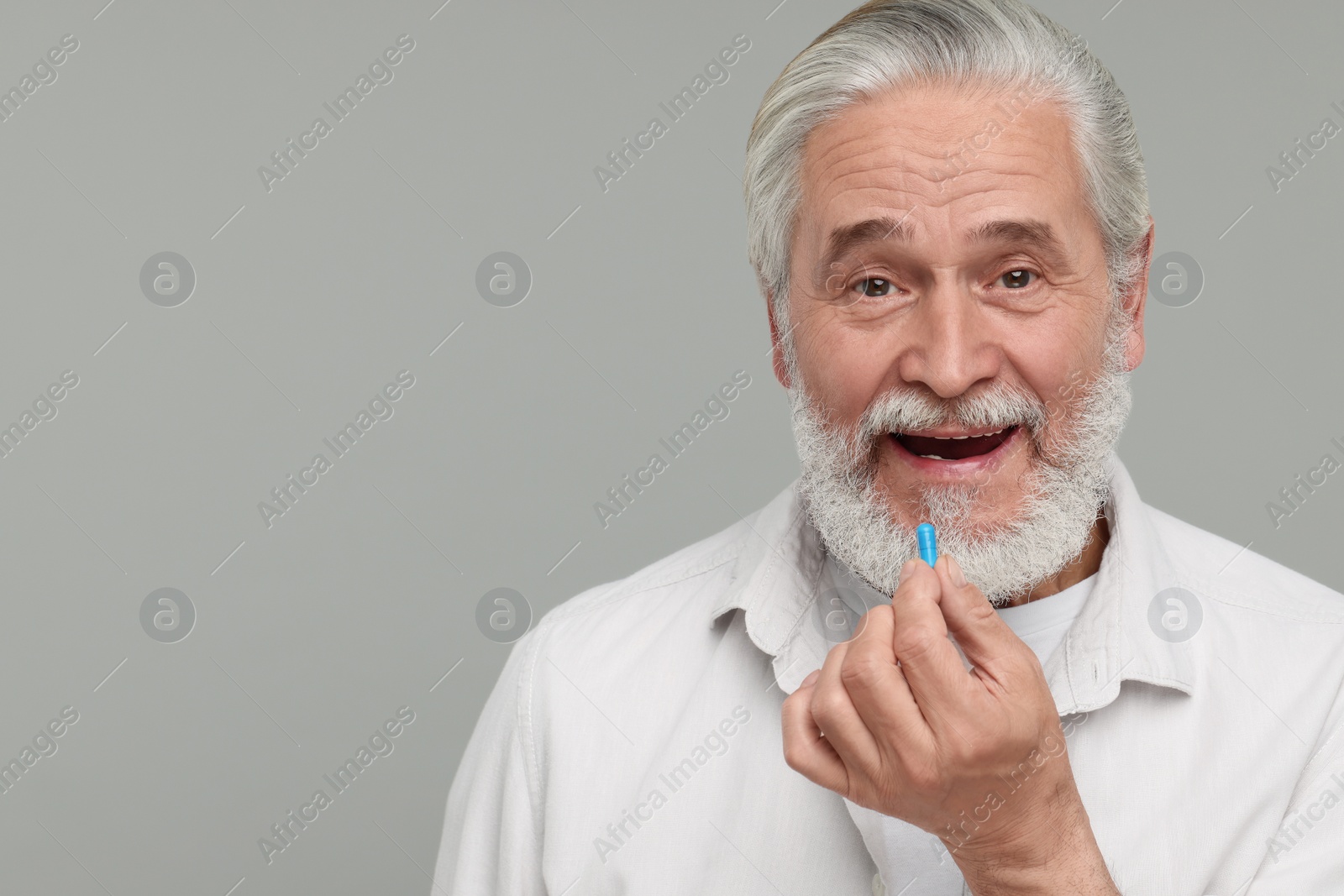 Photo of Senior man taking pill on grey background. Space for text
