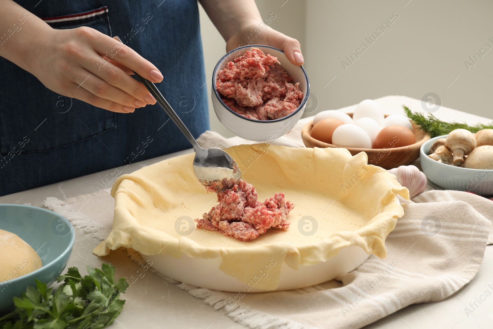 Photo of Woman putting meat into baking dish with dough to make pie at light grey table, closeup