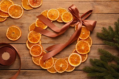 Photo of Decorative wreath made with dry oranges, ribbon and fir branches on wooden table, flat lay