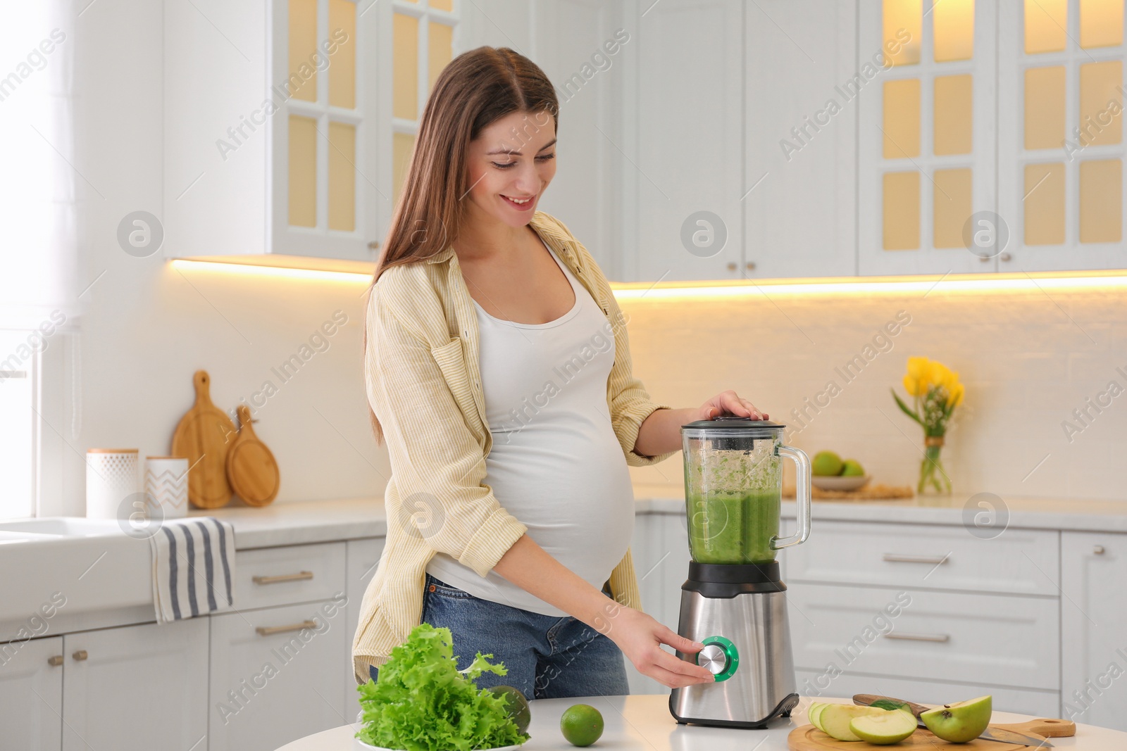 Photo of Young pregnant woman preparing smoothie at table in kitchen. Healthy eating