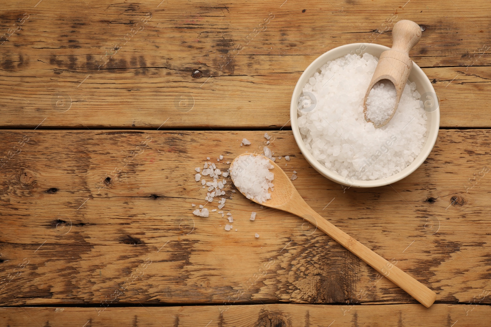 Photo of Bowl, spoon and scoop with sea salt on wooden table, flat lay. Space for text