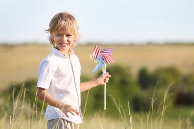 Photo of Cute little boy with pinwheel outdoors, space for text. Child spending time in nature