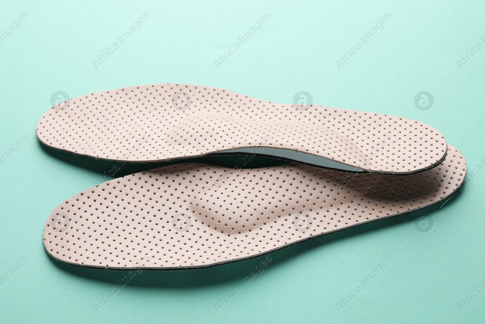 Photo of Beige comfortable orthopedic insoles on turquoise background, closeup