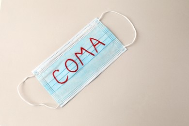 Photo of Medical mask with word Coma on beige background, top view