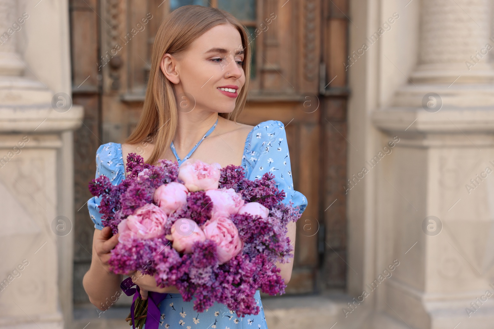 Photo of Beautiful woman with bouquet of spring flowers near building outdoors, space for text