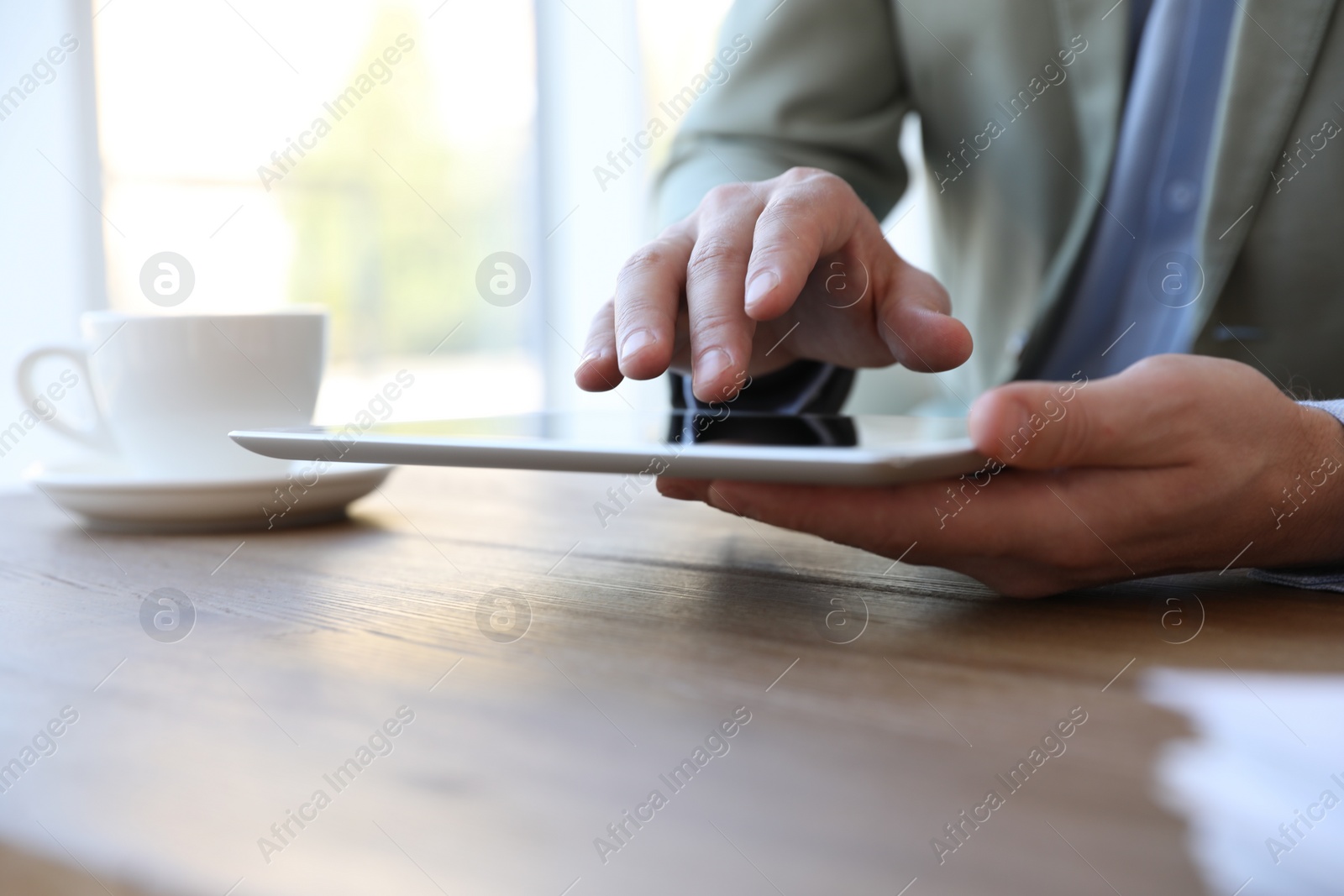 Photo of Businessman working with modern tablet at wooden table in office, closeup