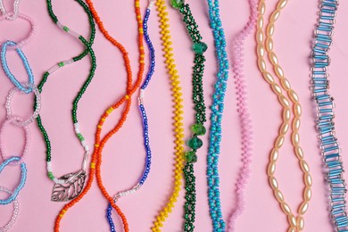Photo of Beautiful handmade beaded necklaces on pink background, flat lay