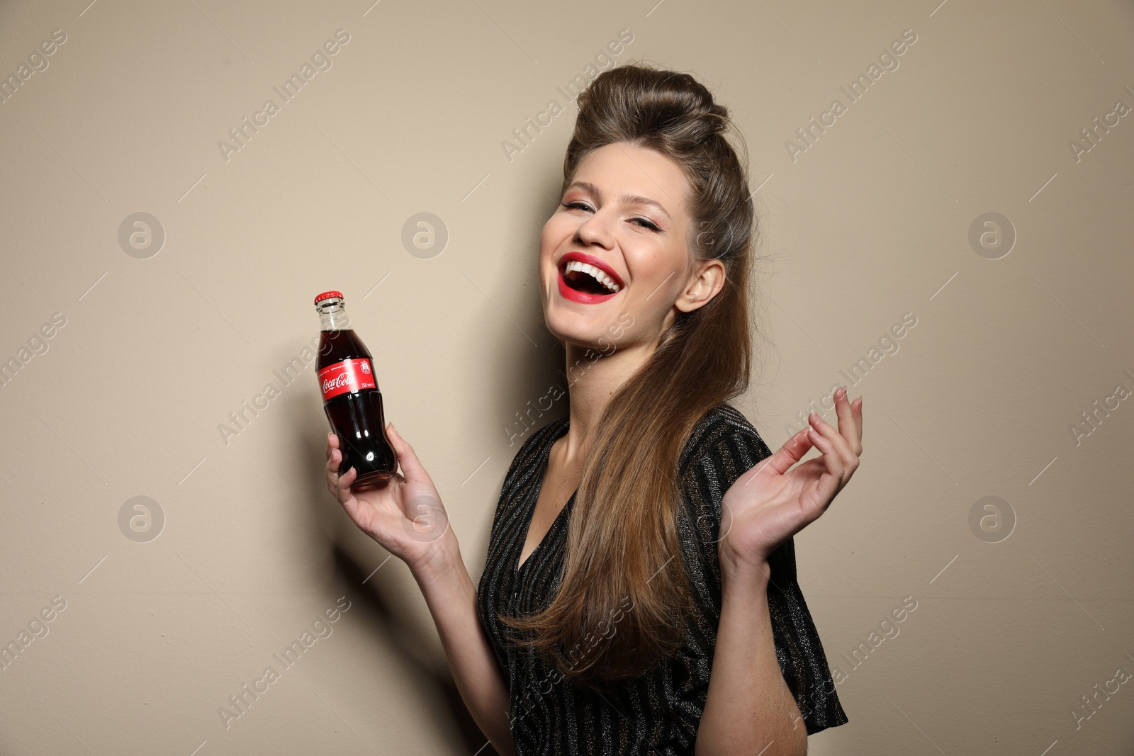 Photo of MYKOLAIV, UKRAINE - NOVEMBER 28, 2018: Young woman with bottle of Coca-Cola on color background