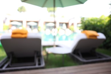 Photo of Sunbeds near swimming pool at luxury resort, blurred view