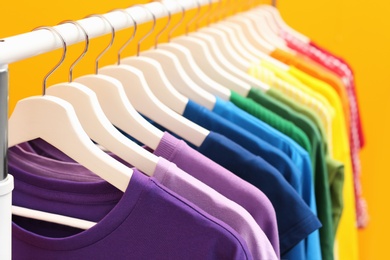 Rack with rainbow clothes on color background