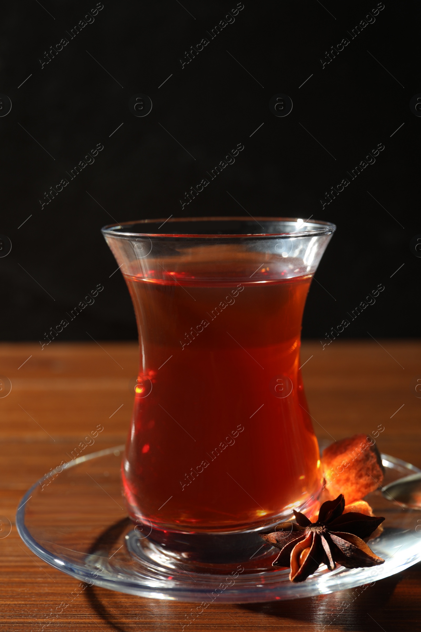 Photo of Glass of traditional Turkish tea on wooden table against black background