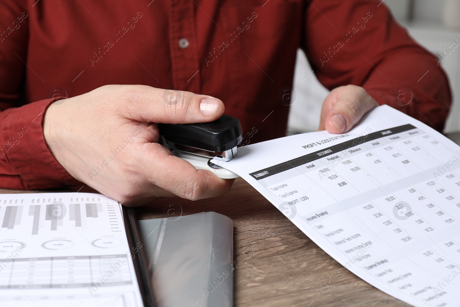 Photo of Man with documents using stapler at wooden table, closeup