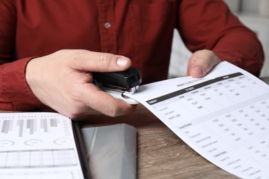 Photo of Man with documents using stapler at wooden table, closeup