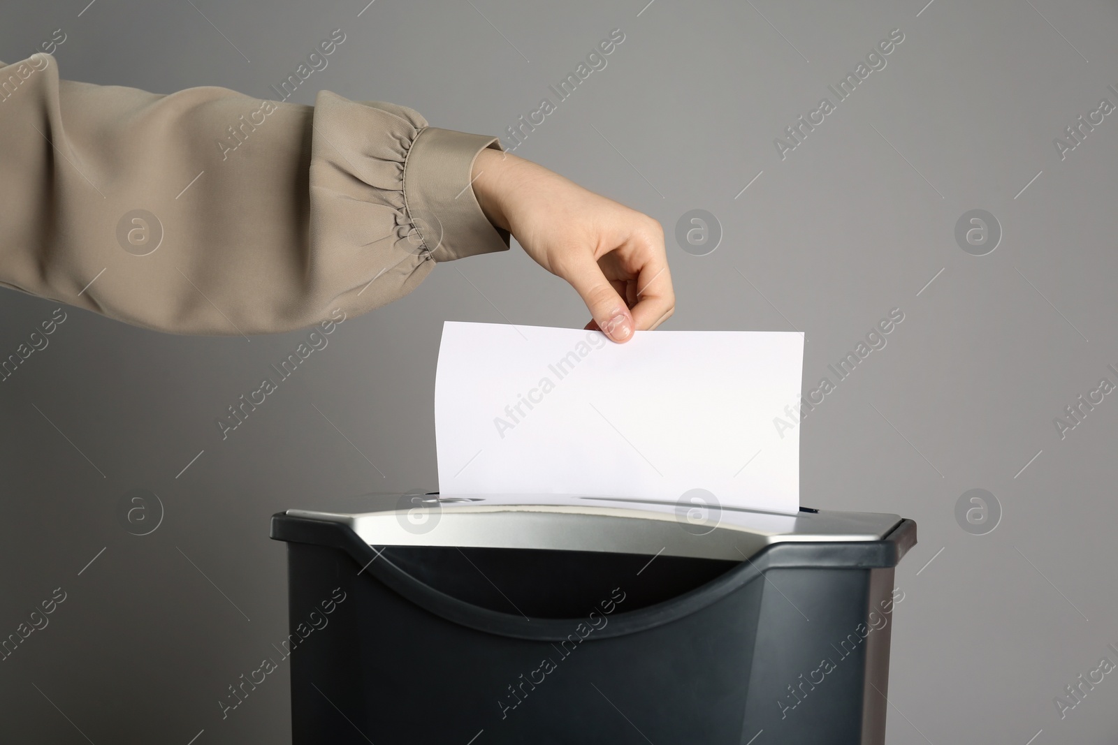Photo of Woman destroying sheet of paper with shredder on grey background, closeup