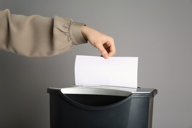 Woman destroying sheet of paper with shredder on grey background, closeup