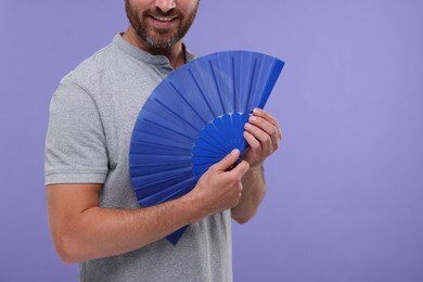 Photo of Man holding hand fan on purple background, closeup. Space for text