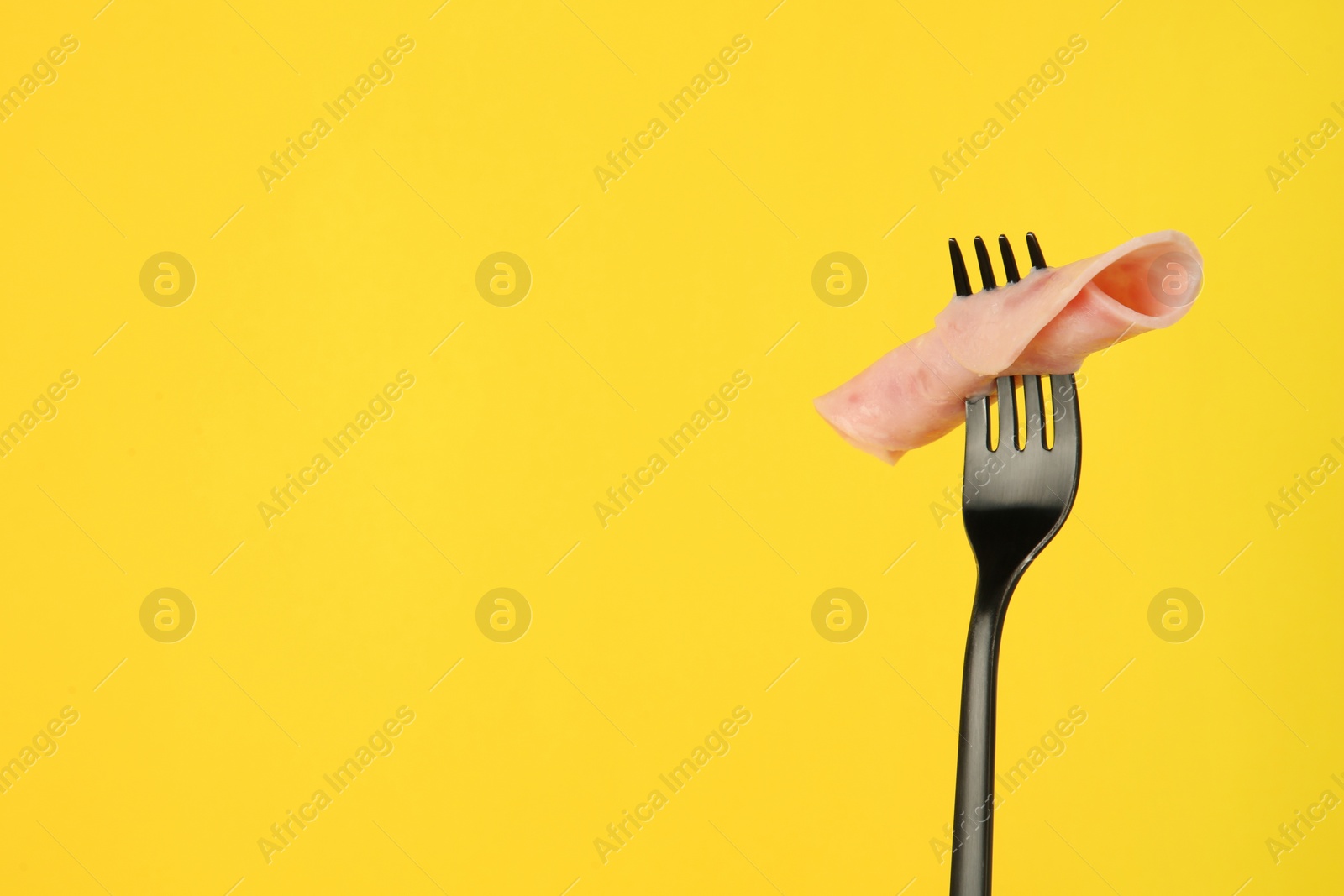 Photo of Fork with tasty slice of ham on yellow background, space for text