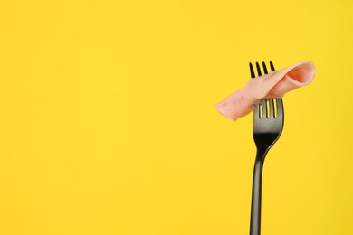 Fork with tasty slice of ham on yellow background, space for text