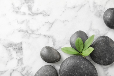 Photo of Black spa stones with green branch on marble background, flat lay. Space for text