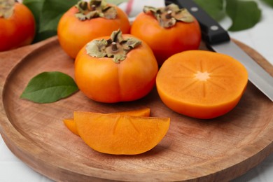 Photo of Whole and cut delicious ripe persimmons on table, closeup
