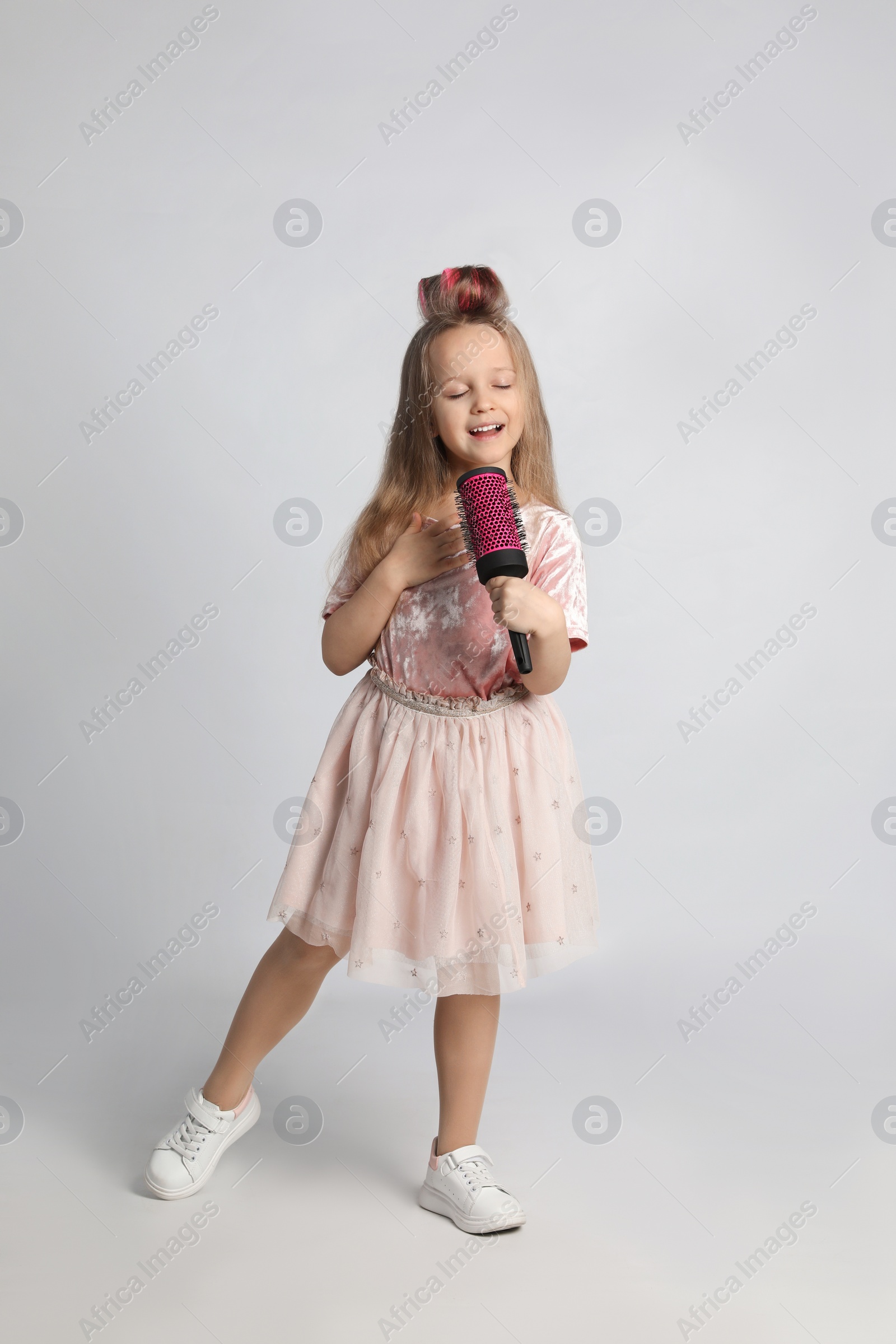 Photo of Cute little girl with hairbrush singing on light grey background