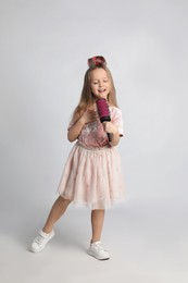 Photo of Cute little girl with hairbrush singing on light grey background