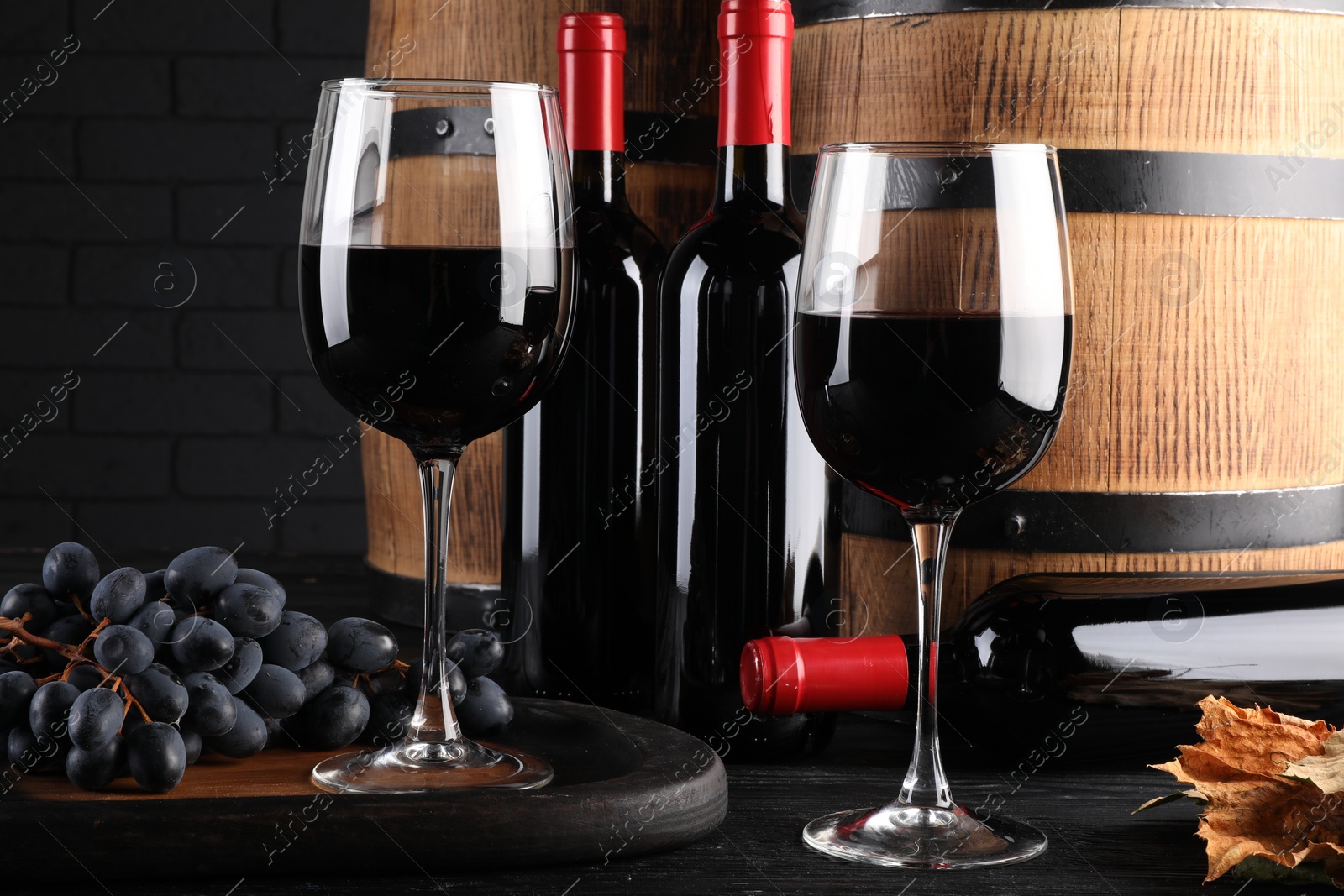 Photo of Delicious wine, wooden barrels and fresh grapes on black table