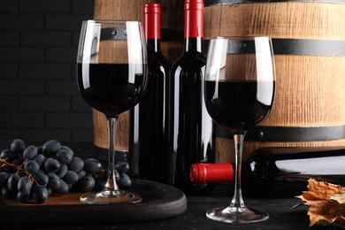 Photo of Delicious wine, wooden barrels and fresh grapes on black table