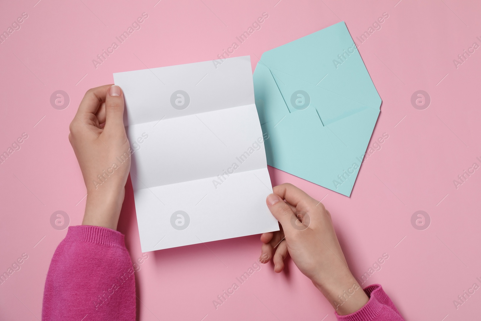 Photo of Woman with blank sheet of paper and envelope at pink table, top view. Space for text